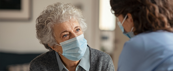 Senior lady and nurse talking while wearing medical masks